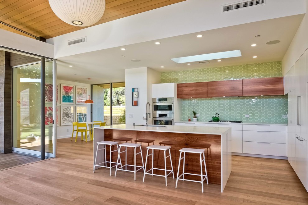 Foto di un cucina con isola centrale moderno con ante lisce, ante bianche, paraspruzzi verde, elettrodomestici in acciaio inossidabile e pavimento in legno massello medio