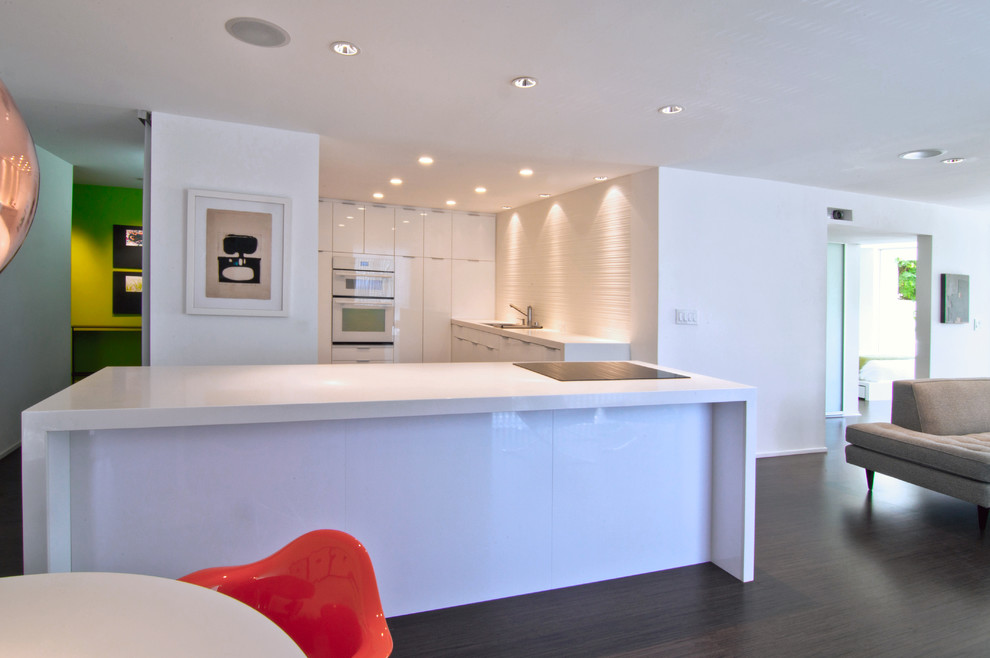 Example of a trendy u-shaped open concept kitchen design in Orange County with an undermount sink, flat-panel cabinets, white cabinets and solid surface countertops