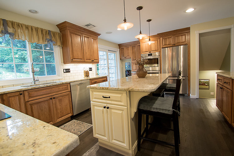 Eat-in kitchen - mid-sized traditional u-shaped dark wood floor eat-in kitchen idea in Bridgeport with an undermount sink, raised-panel cabinets, medium tone wood cabinets, granite countertops, white backsplash, subway tile backsplash, stainless steel appliances and an island