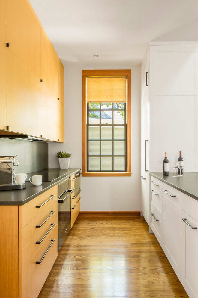 Small traditional galley kitchen/diner in Boston with a single-bowl sink, flat-panel cabinets, light wood cabinets, soapstone worktops, black splashback, black appliances, medium hardwood flooring and brown floors.