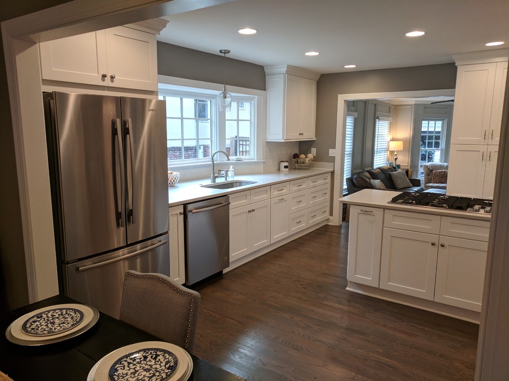 Example of a mid-sized transitional u-shaped dark wood floor and brown floor eat-in kitchen design in Atlanta with an undermount sink, shaker cabinets, white cabinets, solid surface countertops, white backsplash, subway tile backsplash, stainless steel appliances and a peninsula