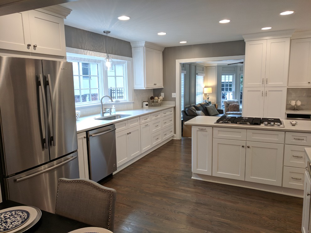 Mid-sized transitional u-shaped dark wood floor and brown floor eat-in kitchen photo in Atlanta with an undermount sink, shaker cabinets, white cabinets, solid surface countertops, white backsplash, subway tile backsplash, stainless steel appliances and a peninsula