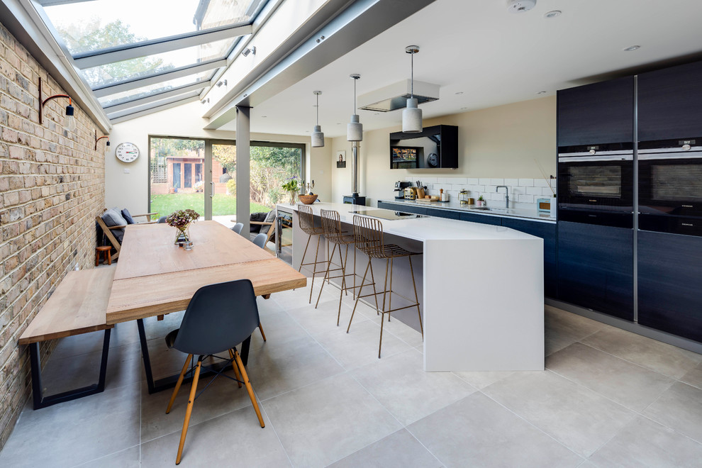 Medium sized contemporary single-wall kitchen in London with a submerged sink, flat-panel cabinets, blue cabinets, stainless steel appliances, slate flooring, an island and grey floors.