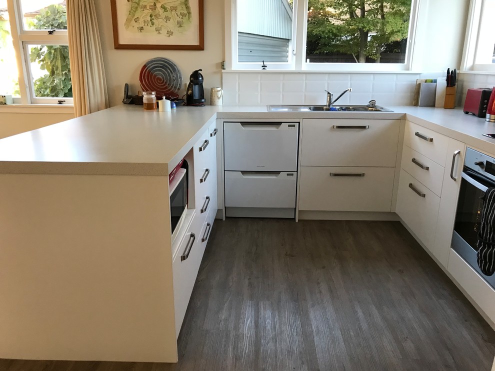Inspiration for a mid-sized contemporary u-shaped vinyl floor and brown floor eat-in kitchen remodel in Christchurch with a double-bowl sink, flat-panel cabinets, white cabinets, laminate countertops, white backsplash, porcelain backsplash, stainless steel appliances, a peninsula and white countertops