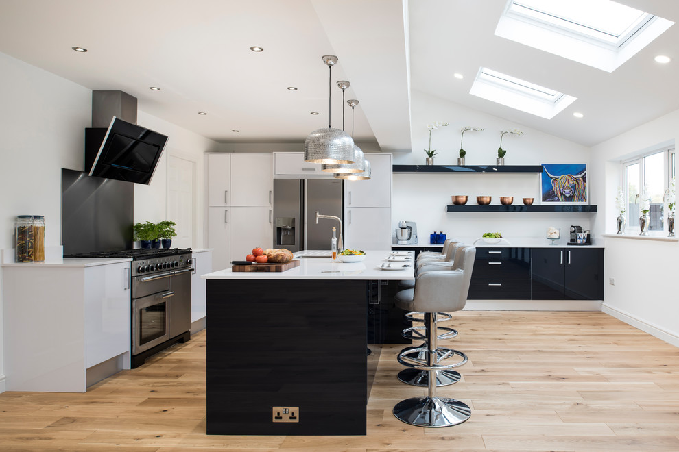 This is an example of a large contemporary l-shaped open plan kitchen in West Midlands with white cabinets, stainless steel appliances, light hardwood flooring, beige floors, white worktops, a submerged sink, flat-panel cabinets, grey splashback and an island.