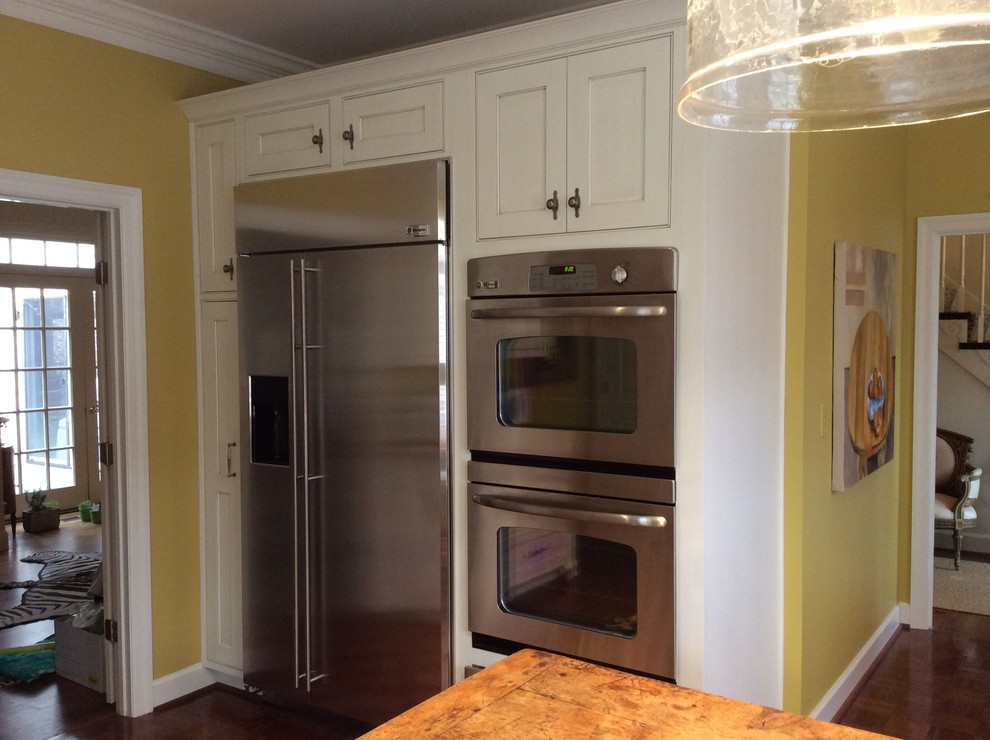 Example of a mid-sized classic medium tone wood floor enclosed kitchen design in Birmingham with a single-bowl sink, beaded inset cabinets, white cabinets, granite countertops, white backsplash, ceramic backsplash, stainless steel appliances and an island
