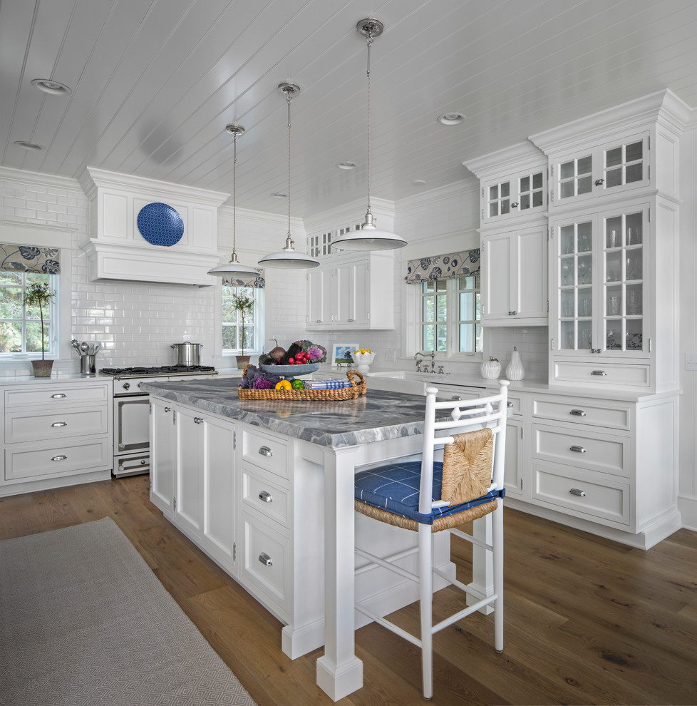 Beach style light wood floor kitchen photo in Other with a farmhouse sink, glass-front cabinets, white cabinets, white backsplash, subway tile backsplash, white appliances and an island