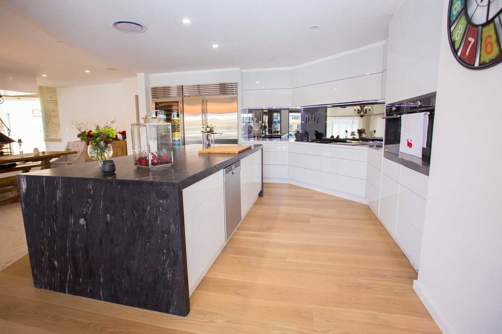 Foto på ett stort funkis kök, med vita skåp, bänkskiva i kvarts, rostfria vitvaror, ljust trägolv och en köksö
