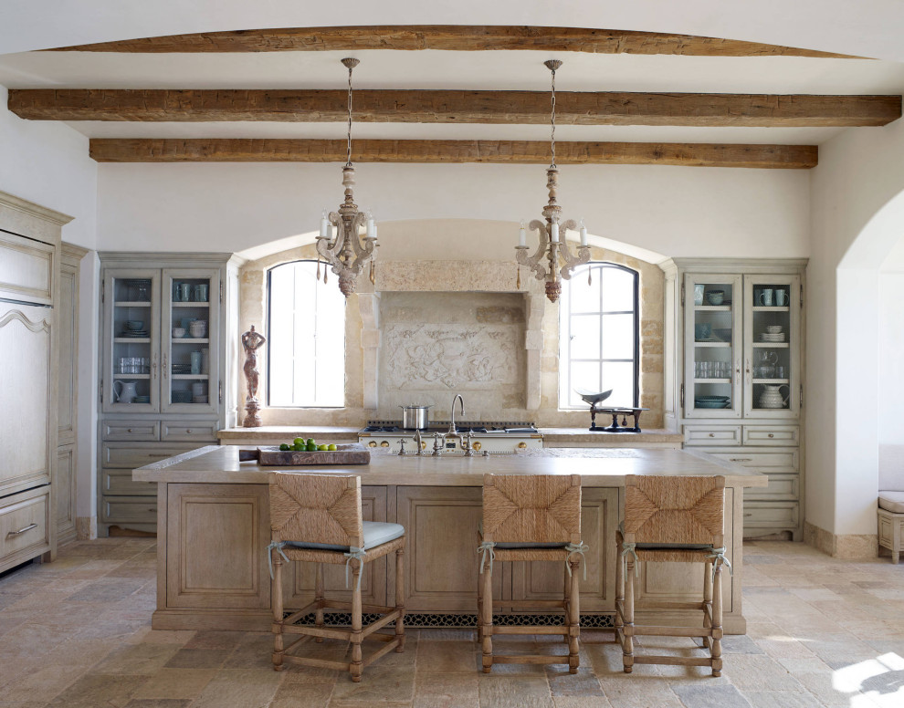 Inspiration for a french country l-shaped beige floor and exposed beam kitchen remodel in Los Angeles with a farmhouse sink, raised-panel cabinets, light wood cabinets, beige backsplash, white appliances, an island and beige countertops