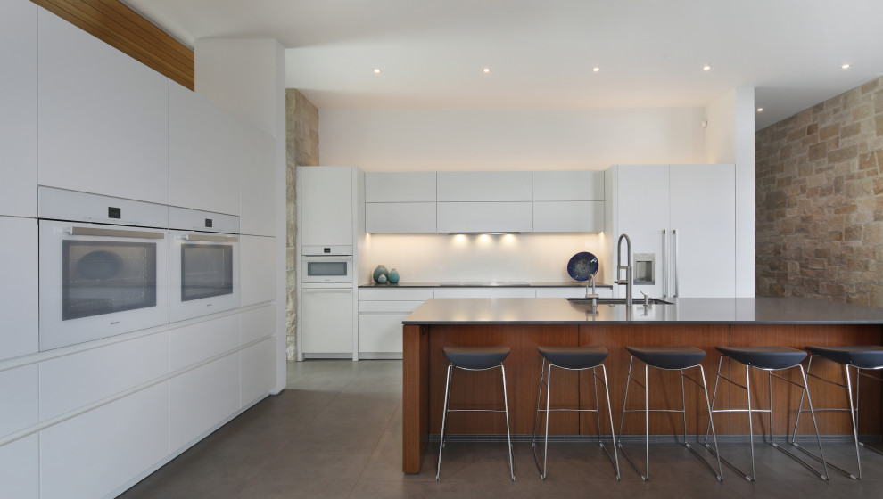 Inspiration for a contemporary l-shaped gray floor kitchen remodel in San Diego with an undermount sink, flat-panel cabinets, white cabinets, white backsplash, white appliances, an island and black countertops