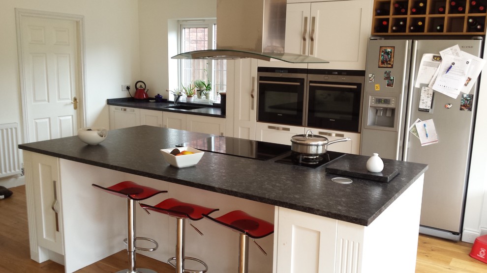 Inredning av ett modernt mellanstort linjärt kök och matrum, med en undermonterad diskho, skåp i shakerstil, vita skåp, granitbänkskiva, grönt stänkskydd, svarta vitvaror, ljust trägolv och en köksö