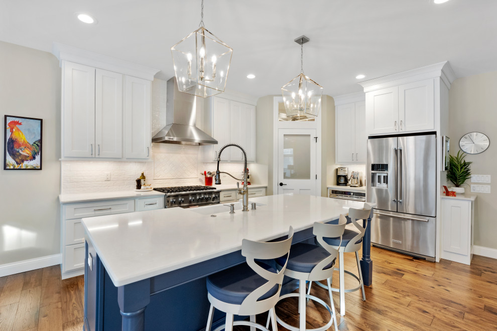 Transitional u-shaped medium tone wood floor and brown floor open concept kitchen photo in Other with a farmhouse sink, shaker cabinets, white cabinets, white backsplash, stainless steel appliances, an island and white countertops