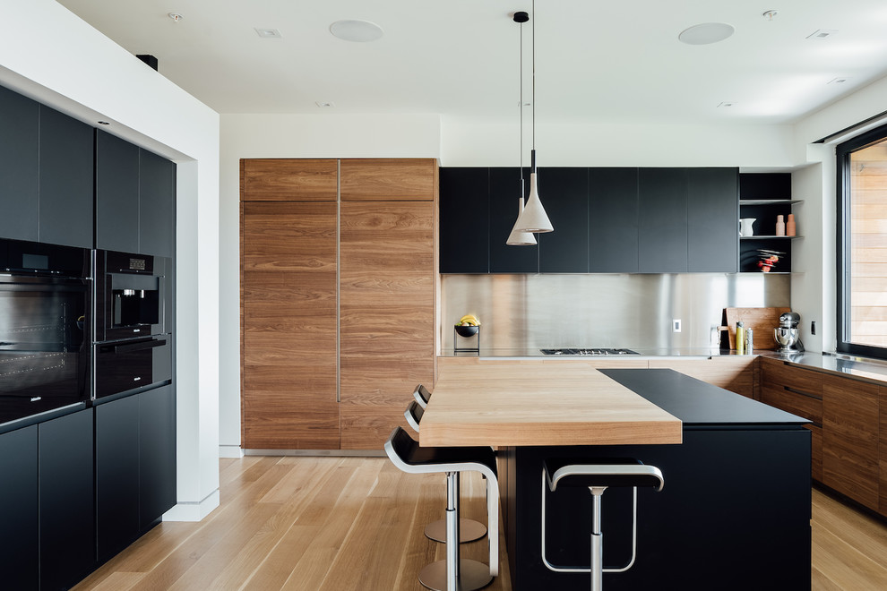 Inspiration för moderna l-kök, med släta luckor, svarta skåp, bänkskiva i rostfritt stål, stänkskydd med metallisk yta, integrerade vitvaror, ljust trägolv, en köksö och beiget golv