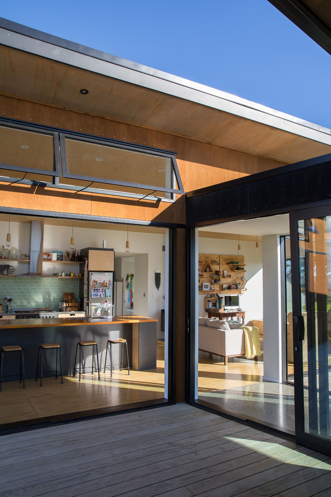 Photo of a scandi galley open plan kitchen in Auckland with a double-bowl sink, flat-panel cabinets, light wood cabinets, wood worktops, green splashback, glass tiled splashback, stainless steel appliances, plywood flooring, an island and brown floors.