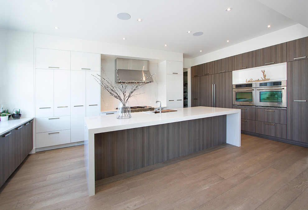 Design ideas for an expansive contemporary u-shaped kitchen/diner in Calgary with a submerged sink, flat-panel cabinets, grey cabinets, engineered stone countertops, white splashback, integrated appliances, light hardwood flooring, an island and white worktops.