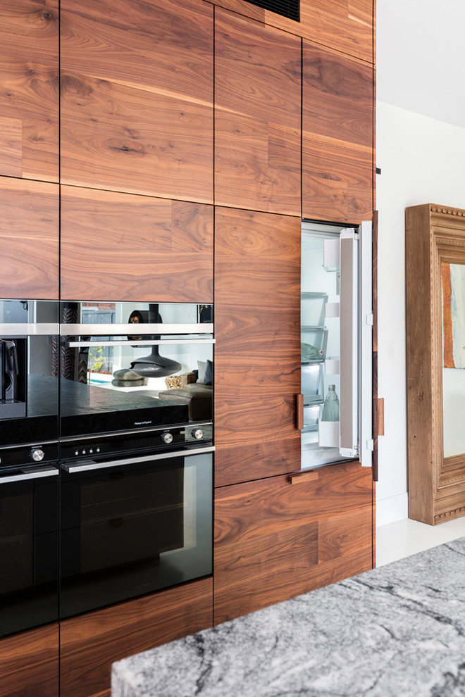シドニーにあるラグジュアリーな広いコンテンポラリースタイルのおしゃれなキッチン (アンダーカウンターシンク、中間色木目調キャビネット、御影石カウンター、白いキッチンパネル、黒い調理設備、白い床) の写真