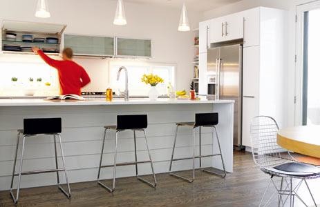 Cette image montre une cuisine américaine parallèle minimaliste avec des portes de placard blanches, un plan de travail en quartz modifié, un évier encastré, un placard à porte vitrée, un électroménager en acier inoxydable et parquet foncé.