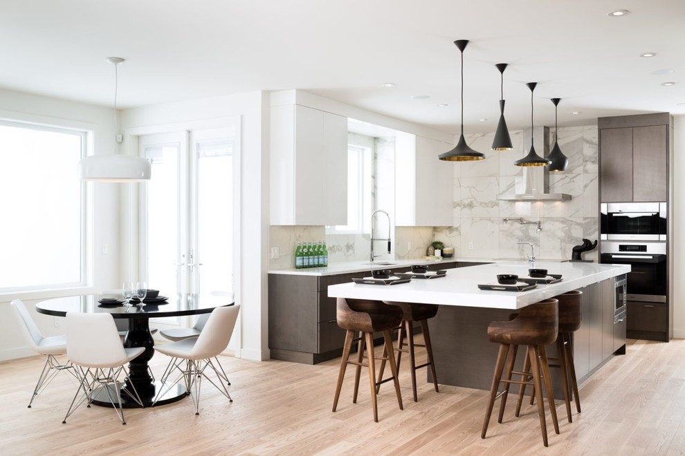 Moderne Wohnküche in L-Form mit Unterbauwaschbecken, flächenbündigen Schrankfronten, dunklen Holzschränken, Küchenrückwand in Weiß, Küchengeräten aus Edelstahl, hellem Holzboden und Kücheninsel in Calgary