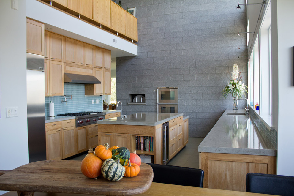 Inredning av ett modernt stort kök, med en undermonterad diskho, skåp i shakerstil, skåp i mellenmörkt trä, bänkskiva i betong, blått stänkskydd, glaspanel som stänkskydd, rostfria vitvaror, klinkergolv i porslin och en köksö
