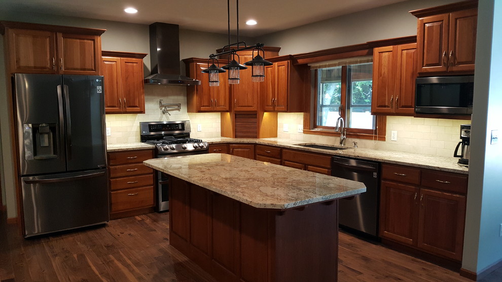 Inspiration for a mid-sized timeless l-shaped medium tone wood floor and brown floor open concept kitchen remodel in Other with an undermount sink, raised-panel cabinets, medium tone wood cabinets, granite countertops, beige backsplash, marble backsplash, stainless steel appliances and an island