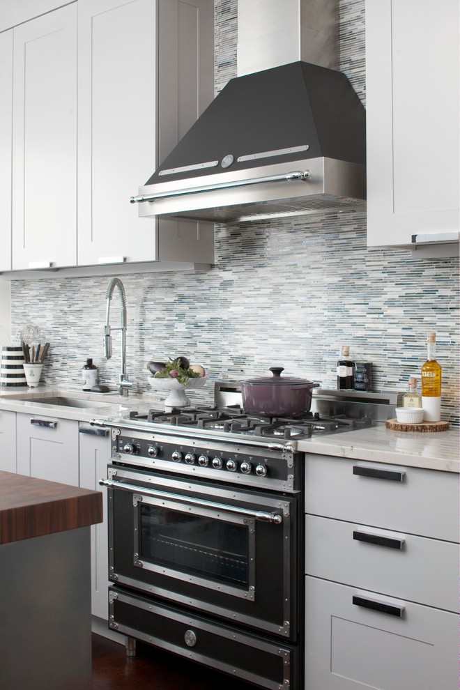 Photo of a contemporary u-shaped kitchen/diner in Boston with a built-in sink, flat-panel cabinets, white cabinets, quartz worktops, grey splashback, stone tiled splashback, stainless steel appliances and an island.