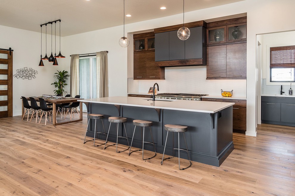 This is an example of a contemporary kitchen/diner in Boise with a submerged sink, flat-panel cabinets, dark wood cabinets, beige splashback, stainless steel appliances, light hardwood flooring, an island and beige worktops.