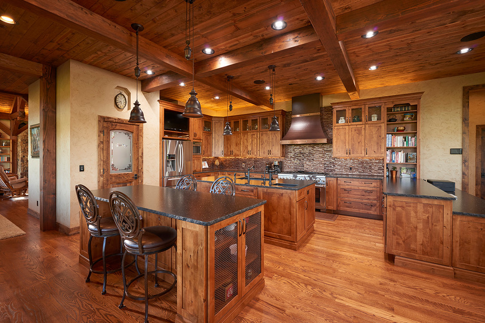 Cette photo montre une cuisine montagne en U et bois brun avec un évier encastré, un placard à porte shaker, une crédence marron, un électroménager en acier inoxydable, un sol en bois brun et 2 îlots.