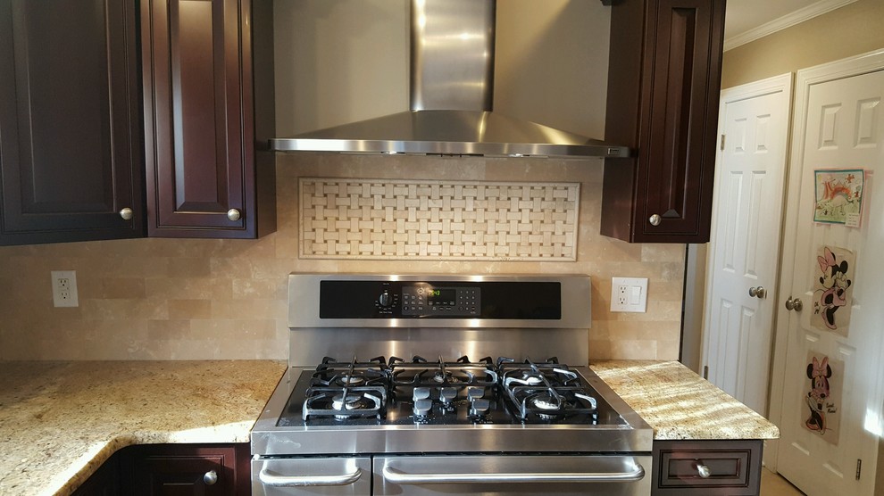 Klassisk inredning av ett avskilt beige beige l-kök, med luckor med upphöjd panel, skåp i mörkt trä, granitbänkskiva, brunt stänkskydd, stänkskydd i travertin och rostfria vitvaror