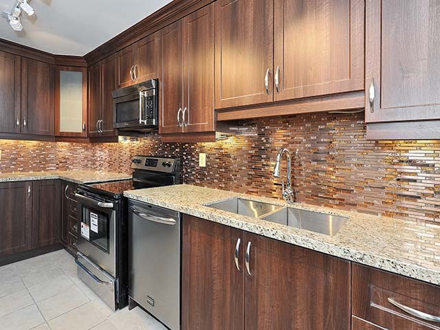 Inspiration for an eclectic l-shaped kitchen remodel in Toronto with a double-bowl sink, recessed-panel cabinets, medium tone wood cabinets, granite countertops, brown backsplash and glass tile backsplash