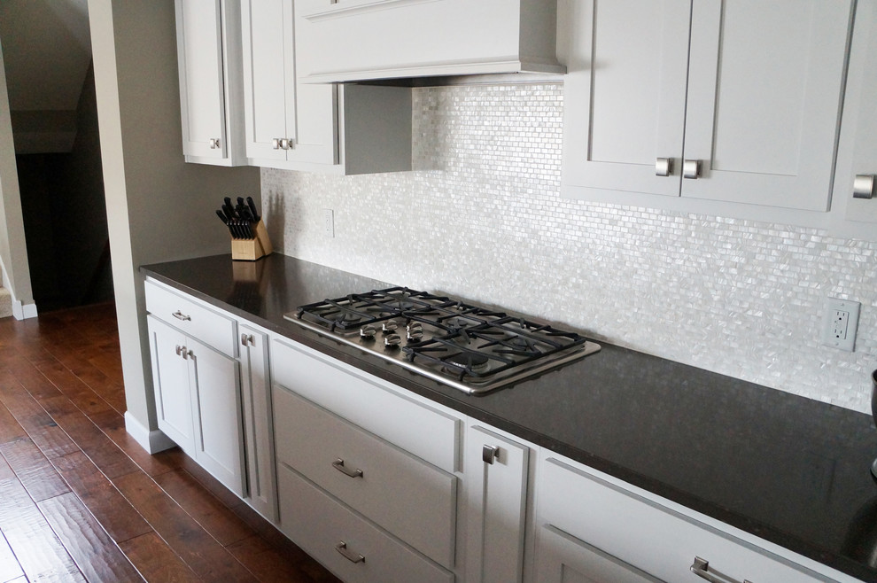 Imagen de cocina costera con puertas de armario blancas, encimera de granito, salpicadero blanco, salpicadero con mosaicos de azulejos y electrodomésticos de acero inoxidable