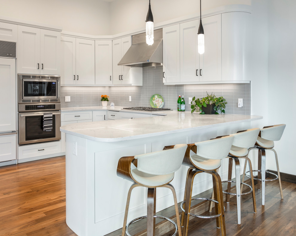 Kitchen - transitional u-shaped medium tone wood floor and brown floor kitchen idea in Salt Lake City with shaker cabinets, white cabinets, gray backsplash, glass tile backsplash, a peninsula and white countertops