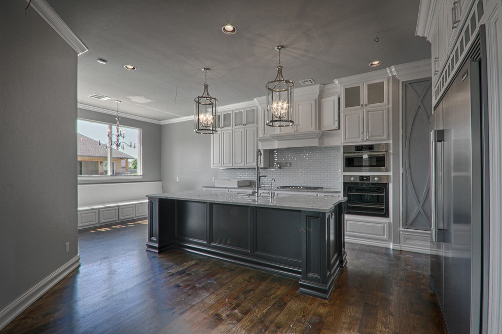 Example of a mid-sized transitional dark wood floor kitchen design in Oklahoma City with an undermount sink, raised-panel cabinets, gray cabinets, granite countertops, white backsplash, glass tile backsplash and stainless steel appliances