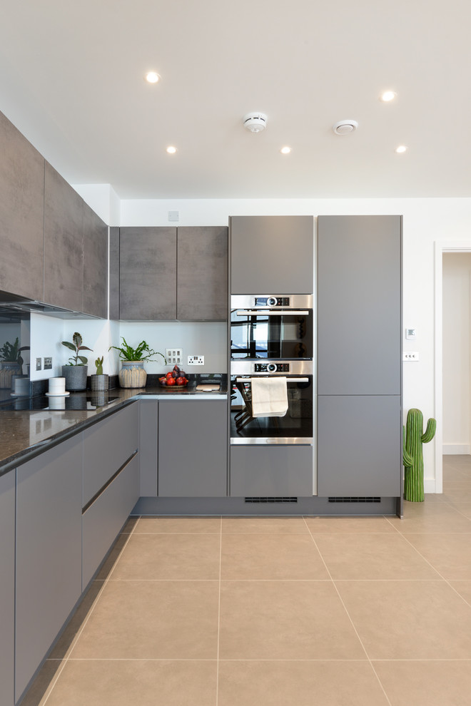 This is an example of a bohemian l-shaped kitchen in London with flat-panel cabinets, grey cabinets, integrated appliances, no island, beige floors and black worktops.