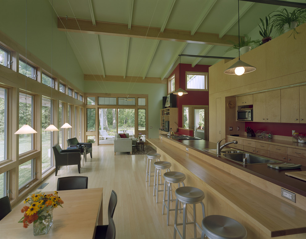 Cette photo montre une cuisine ouverte parallèle moderne en bois clair avec un évier posé, un placard à porte plane et une crédence rouge.