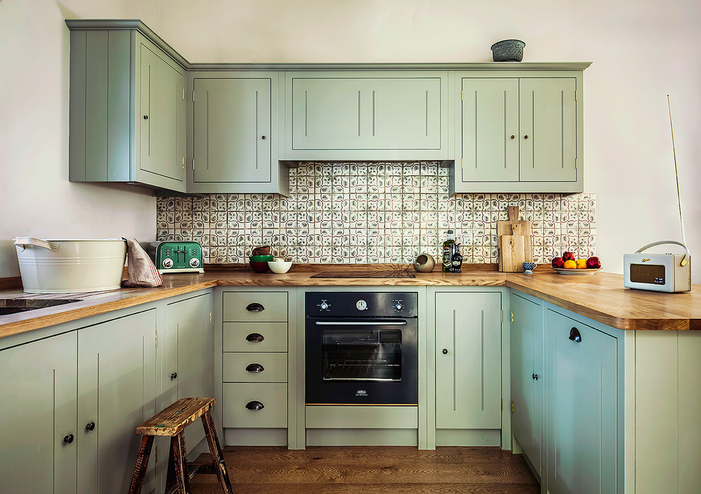 Inspiration for a country u-shaped medium tone wood floor kitchen remodel in London with an undermount sink, beaded inset cabinets, green cabinets, wood countertops, green backsplash, mosaic tile backsplash and black appliances