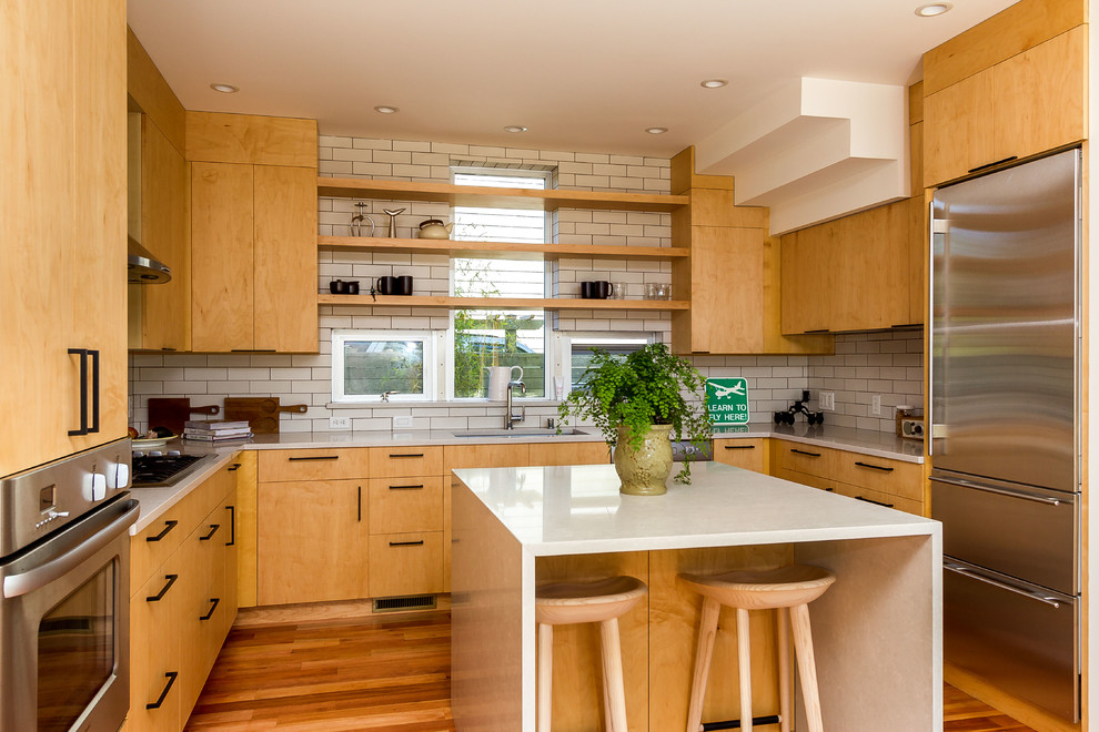 Photo of a medium sized contemporary u-shaped kitchen/diner in Seattle with flat-panel cabinets, light wood cabinets, engineered stone countertops, grey splashback, metro tiled splashback, stainless steel appliances, light hardwood flooring, an island and brown floors.