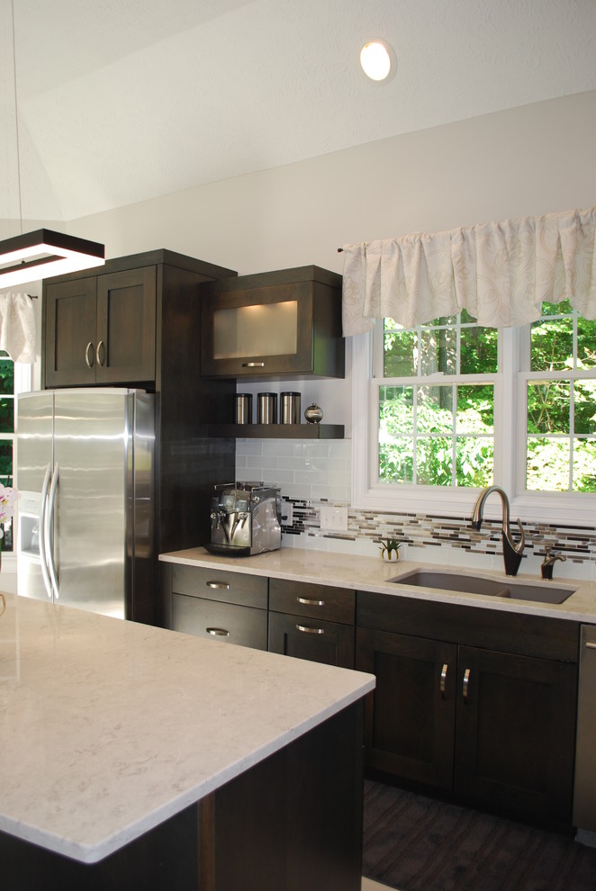 Modern inredning av ett stort l-kök, med en undermonterad diskho, luckor med infälld panel, grå skåp, bänkskiva i kvarts, vitt stänkskydd, stänkskydd i glaskakel, rostfria vitvaror, klinkergolv i porslin och en köksö