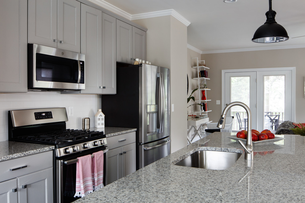 Bild på ett eklektiskt grå grått kök med öppen planlösning, med en undermonterad diskho, luckor med infälld panel, grå skåp, granitbänkskiva, vitt stänkskydd, stänkskydd i keramik, rostfria vitvaror, laminatgolv, en köksö och svart golv