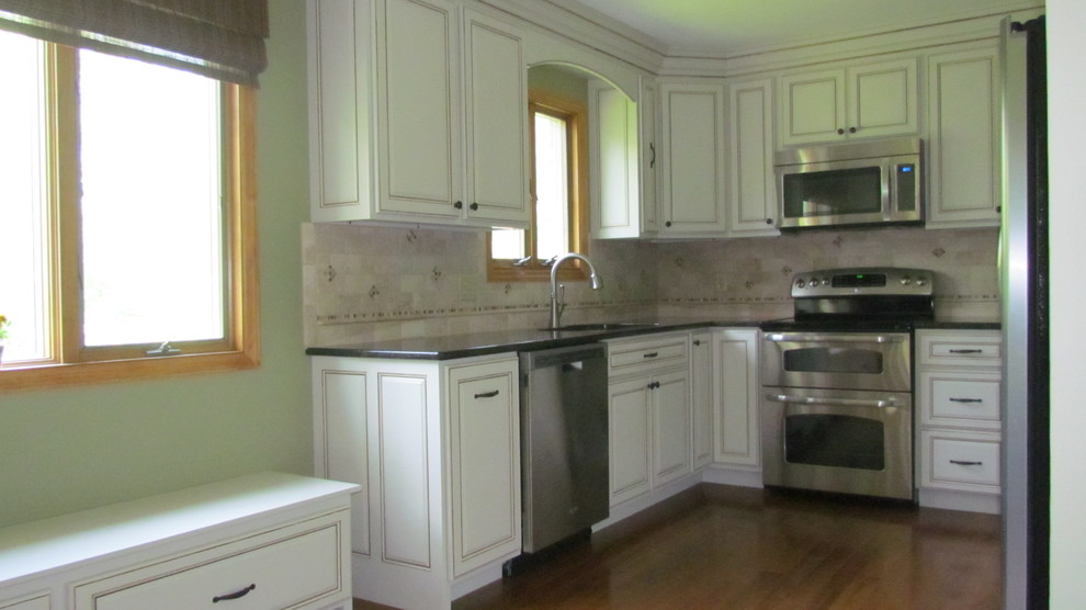 Example of a classic medium tone wood floor eat-in kitchen design in Cincinnati with raised-panel cabinets, white cabinets, granite countertops, beige backsplash and stainless steel appliances