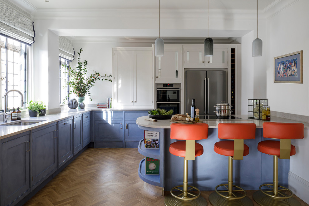 Medium sized classic u-shaped kitchen in London with a submerged sink, blue cabinets, stainless steel appliances, beige floors, shaker cabinets, medium hardwood flooring and a breakfast bar.
