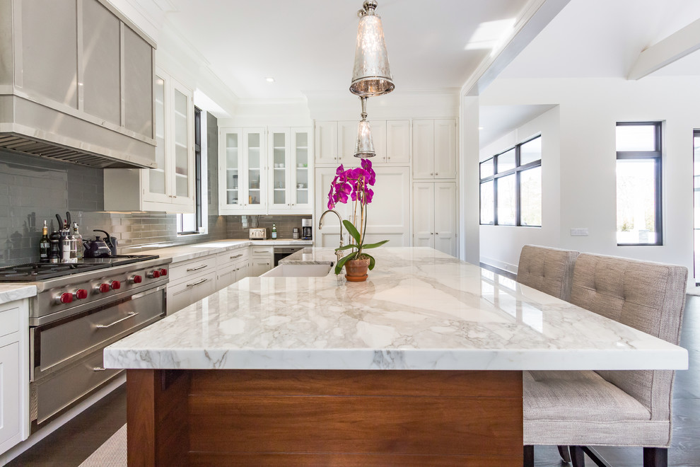 Example of a large transitional u-shaped dark wood floor kitchen design in Other with a farmhouse sink, white cabinets, marble countertops, gray backsplash, subway tile backsplash, stainless steel appliances and an island