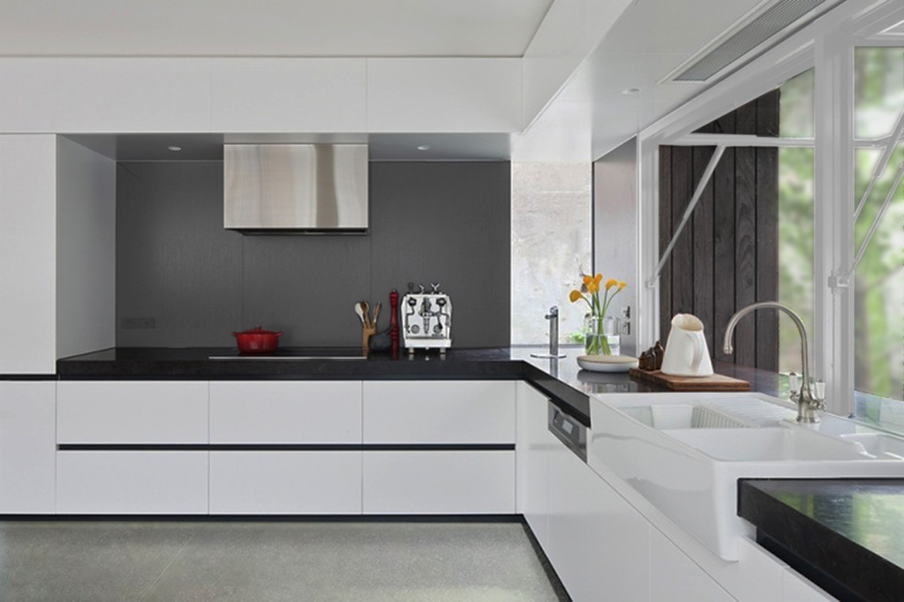 Modern inredning av ett mellanstort kök, med en rustik diskho, släta luckor, vita skåp, granitbänkskiva, grått stänkskydd, stänkskydd i cementkakel, rostfria vitvaror, betonggolv och grått golv