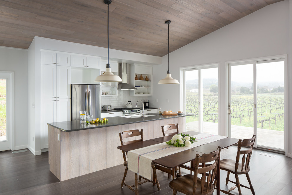 Example of a cottage galley medium tone wood floor eat-in kitchen design in San Francisco with a double-bowl sink, shaker cabinets, white cabinets, white backsplash, subway tile backsplash, stainless steel appliances and an island