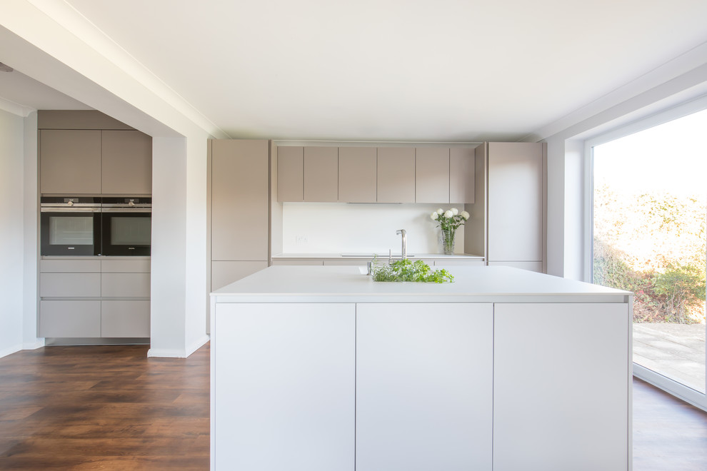 This is an example of a medium sized contemporary kitchen/diner in Sussex with a built-in sink, flat-panel cabinets, white cabinets, composite countertops, stainless steel appliances and an island.