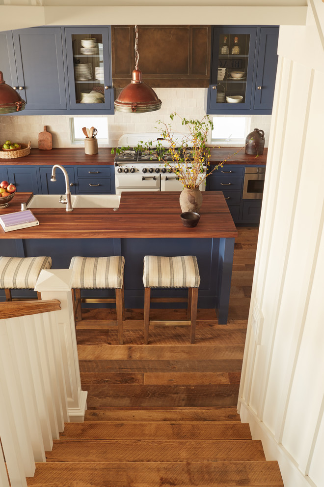 Inspiration for a small coastal l-shaped medium tone wood floor open concept kitchen remodel in Orange County with an island, a farmhouse sink, raised-panel cabinets, blue cabinets, wood countertops, white backsplash, terra-cotta backsplash and paneled appliances