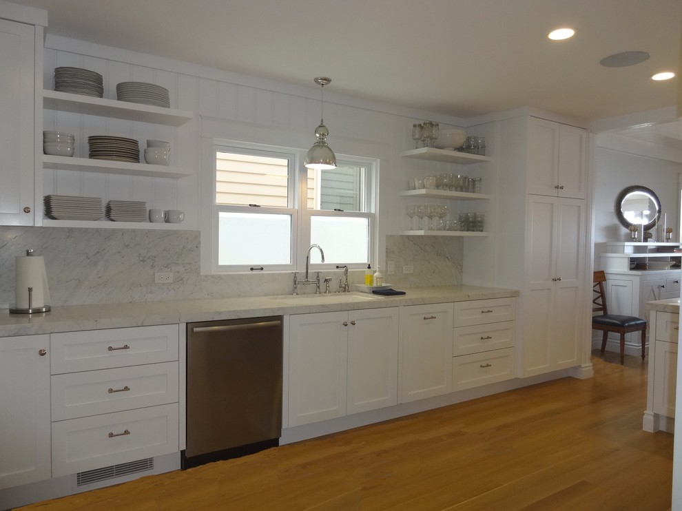 Bild på ett mellanstort maritimt grå grått kök, med en undermonterad diskho, skåp i shakerstil, vita skåp, stänkskydd i sten, rostfria vitvaror, ljust trägolv, grått stänkskydd och beiget golv