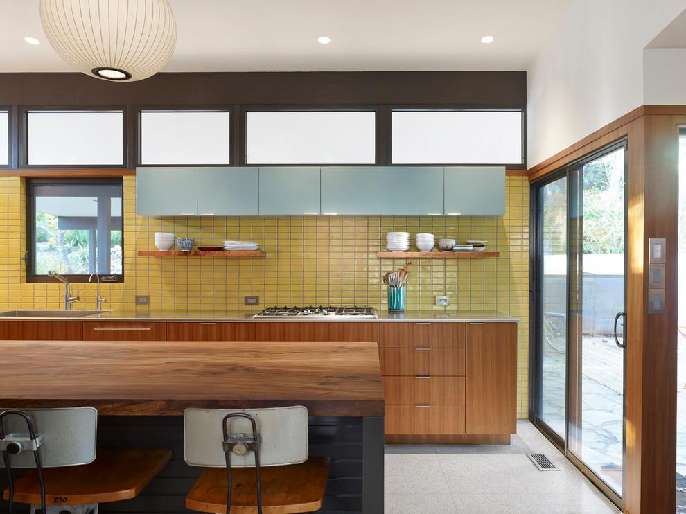 Design ideas for a medium sized midcentury galley kitchen in Austin with an integrated sink, flat-panel cabinets, medium wood cabinets, stainless steel worktops, white splashback, an island and terrazzo flooring.