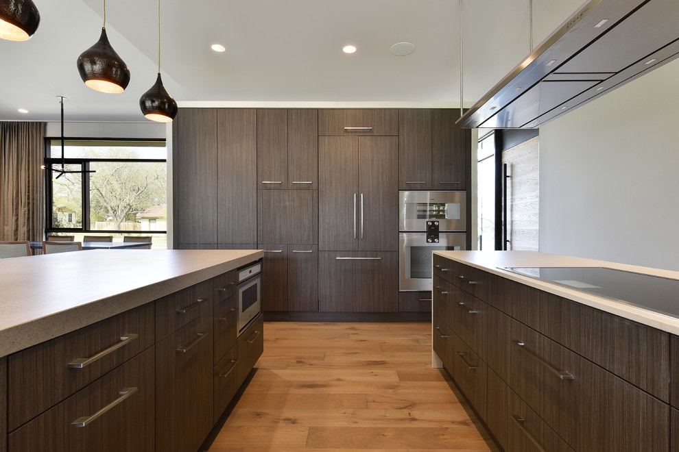 Moderne Küche mit flächenbündigen Schrankfronten, dunklen Holzschränken, Küchengeräten aus Edelstahl, braunem Holzboden und Kücheninsel in Austin