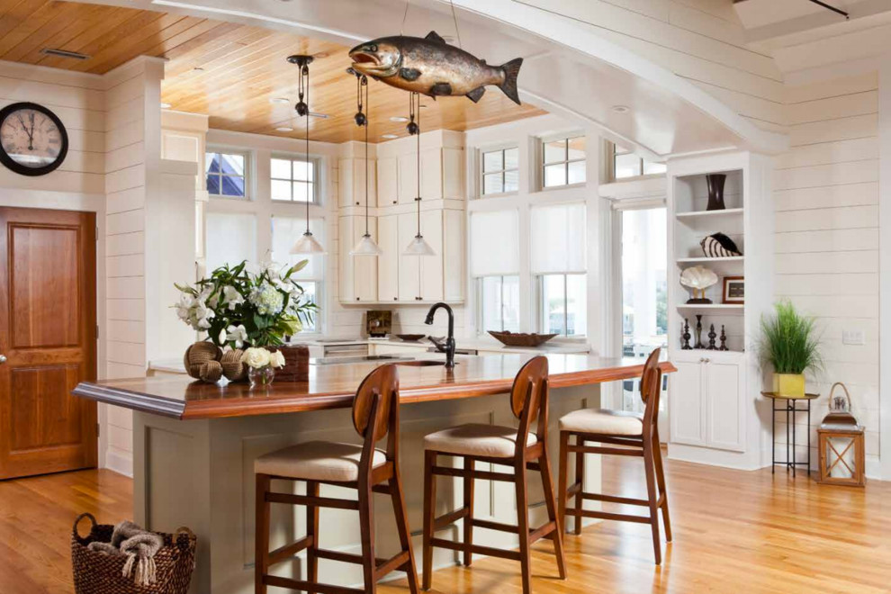 Bild på ett stort maritimt kök, med en undermonterad diskho, luckor med infälld panel, vita skåp, träbänkskiva, vitt stänkskydd, stänkskydd i trä, rostfria vitvaror, mellanmörkt trägolv, en köksö och brunt golv