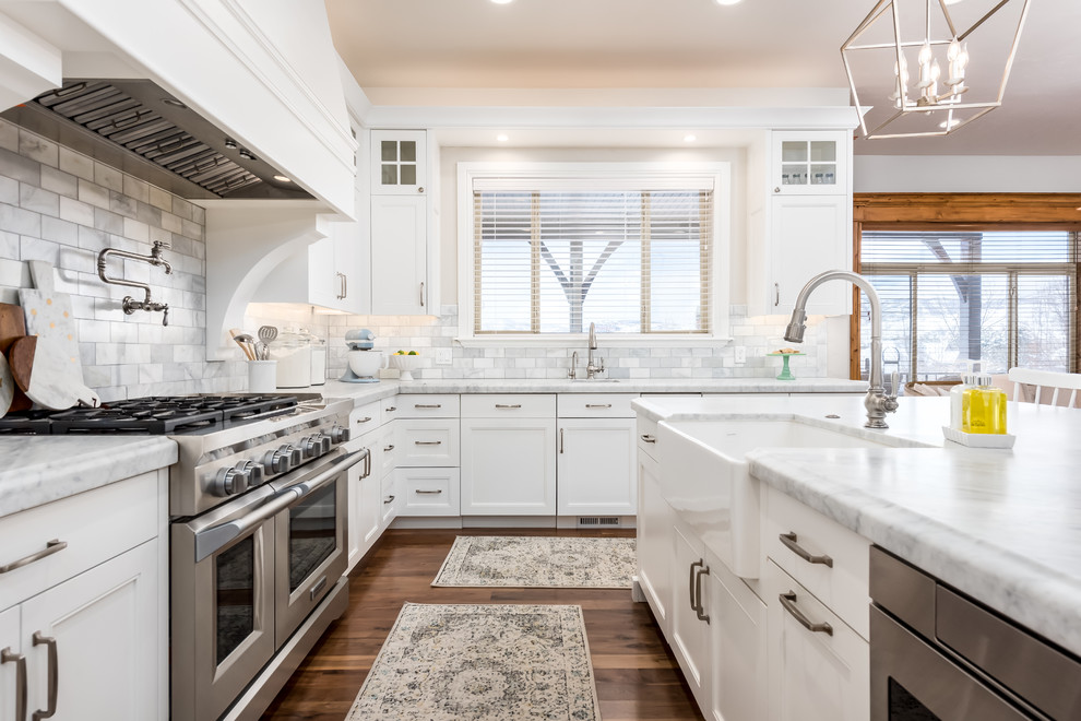 Inspiration for a mid-sized transitional medium tone wood floor and brown floor kitchen remodel in Salt Lake City with a farmhouse sink, white cabinets, marble countertops, gray backsplash, marble backsplash, paneled appliances, an island, white countertops and recessed-panel cabinets